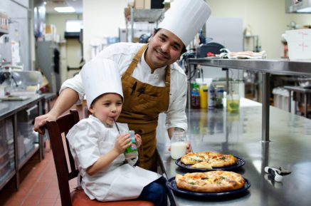 Child and chef cooking pizza together
